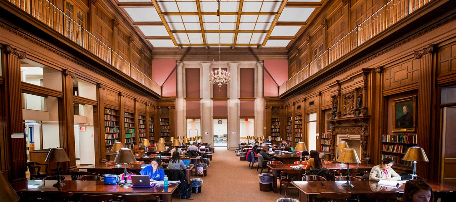 Students working at long tables in a wood-paneled campus library.